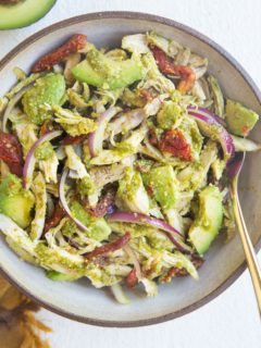 large bowl of pesto chicken salad with avocado, red onion and sun-dried tomatoes.