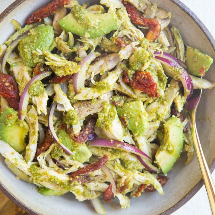 large bowl of pesto chicken salad with avocado, red onion and sun-dried tomatoes.