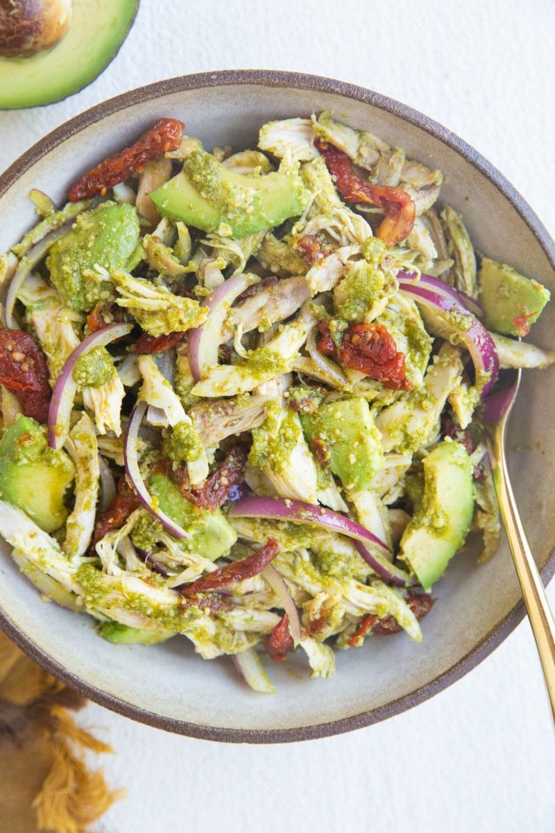 large bowl of pesto chicken salad with avocado, red onion and sun-dried tomatoes.