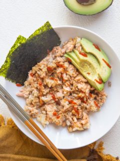 White bowl of salmon and rice mixed together with avocado and seaweed snacks on the side.