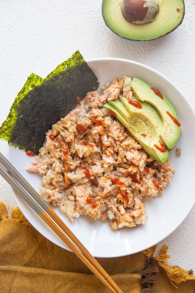 White bowl of salmon and rice mixed together with avocado and seaweed snacks on the side.