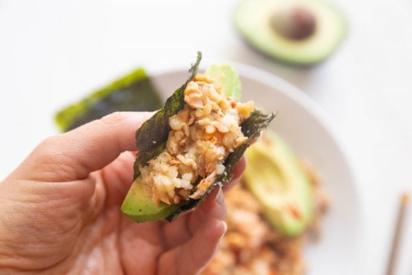 Hand holding dried seaweed snack with rice, salmon and avocado inside