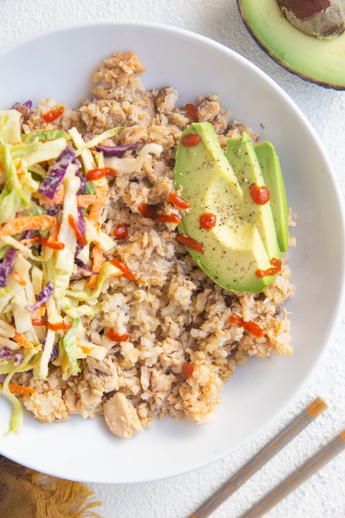 Salmon and rice mixed together in a white bowl with avocado and coleslaw.