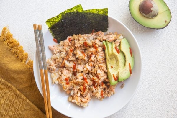 horizontal photo of salmon and rice bowl with roasted seaweed snacks and avocado and a drizzle of sriracha