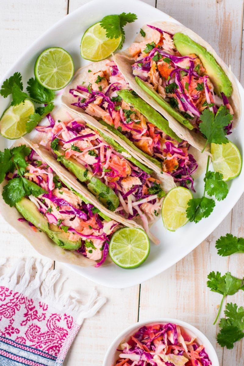 Top down photo of four fish tacos on a platter with coleslaw to the side.