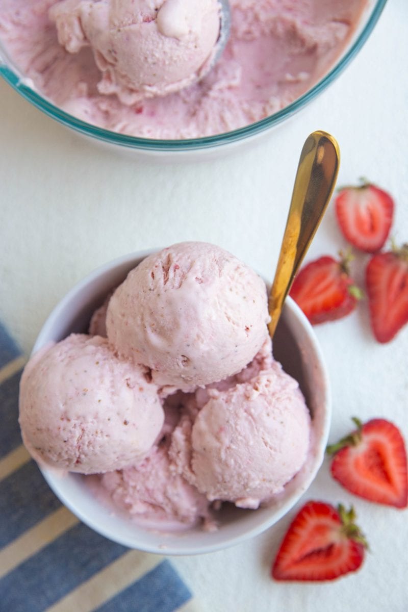 top down photograph of a bowl of strawberry ice cream with fresh strawberries to the side and a blue striped napkin.