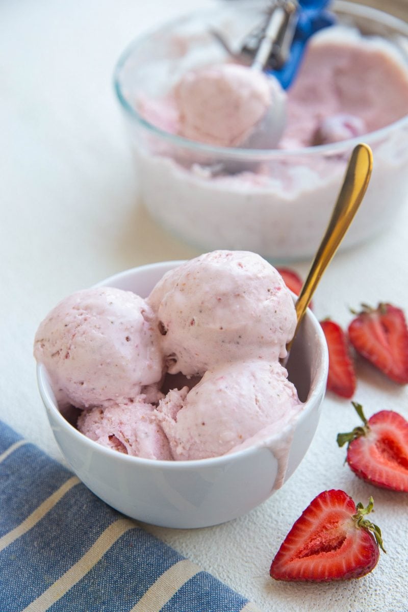 bowl of strawberry ice cream with several scoops and a drip down the side.