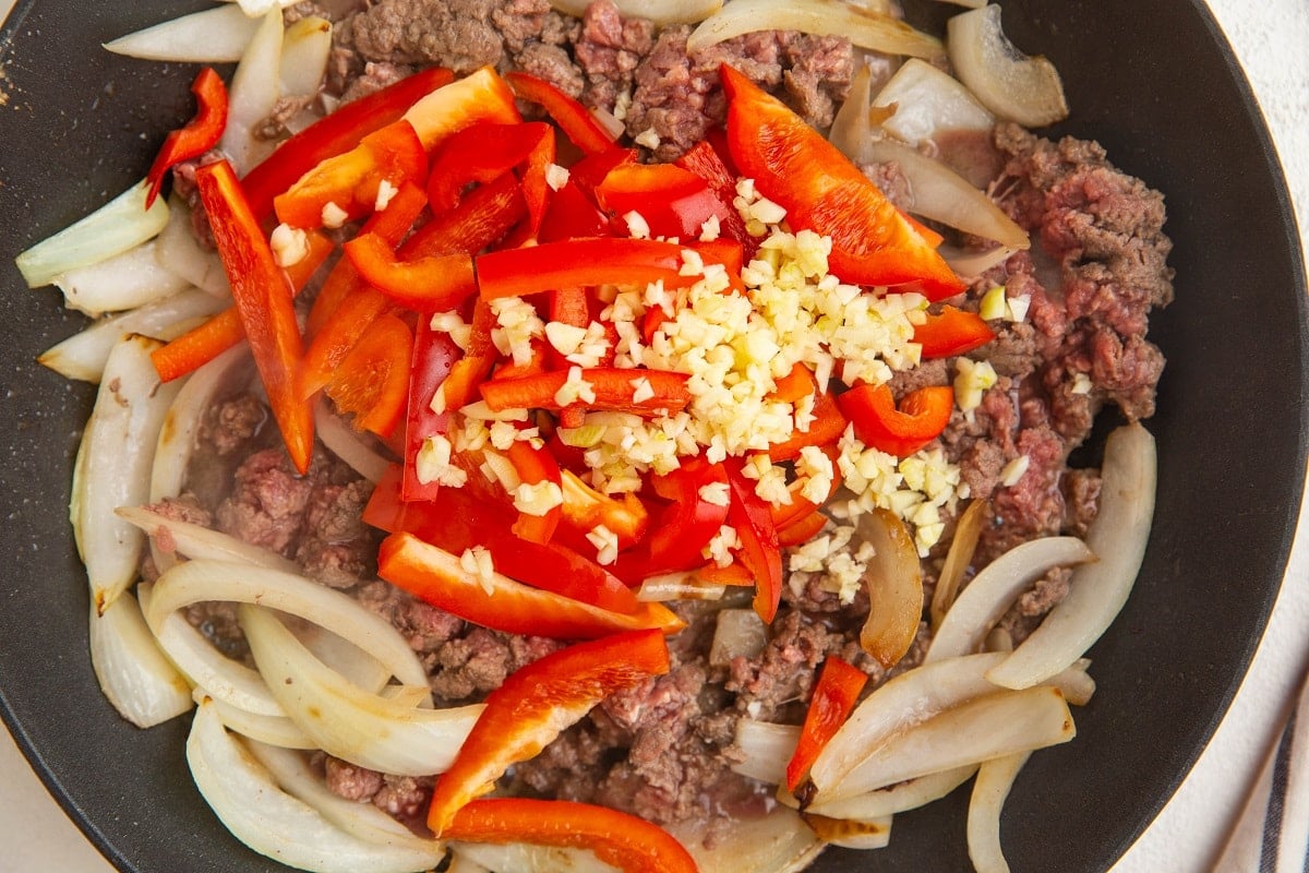 onions, beef, bell pepper, and garlic cooking in a skillet