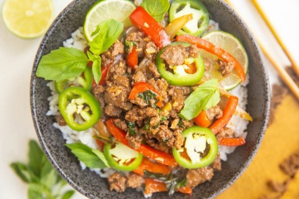 Horizontal photo of black bowl of rice, basil beef, with limes and jalapenos