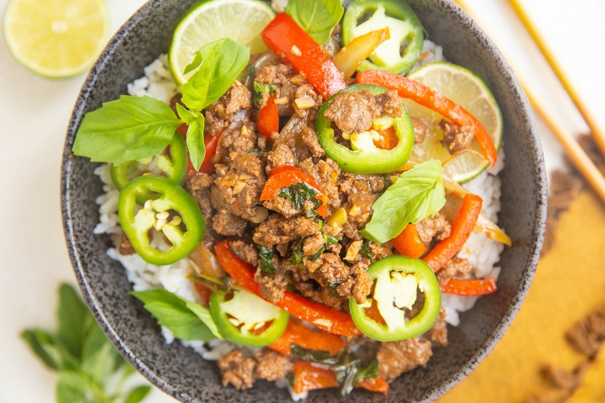 Horizontal photo of black bowl of rice, basil beef, with limes and jalapenos