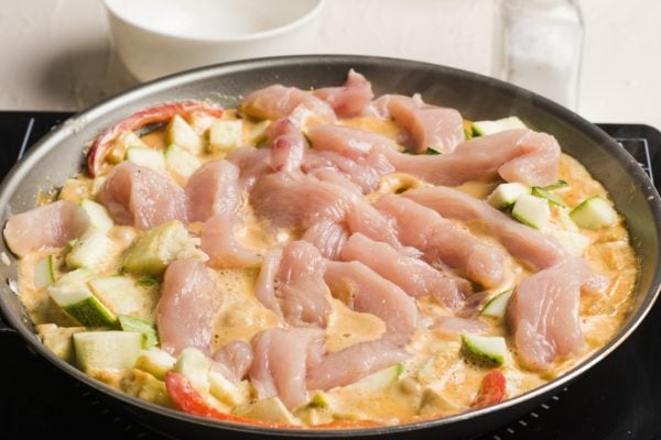 Raw chicken being added in with the vegetables and red curry sauce.