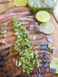 Finished skirt steak on a cutting board sliced up drizzled with chimichurri sauce.