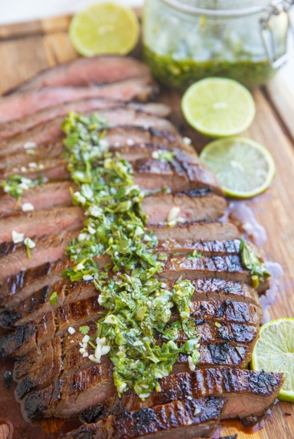 Finished skirt steak on a cutting board sliced up drizzled with chimichurri sauce.