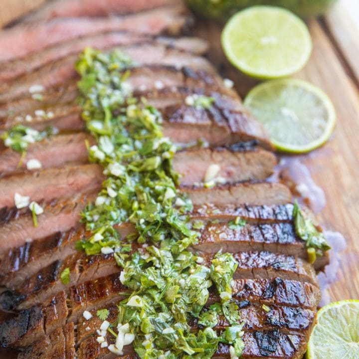 Finished skirt steak on a cutting board sliced up drizzled with chimichurri sauce.