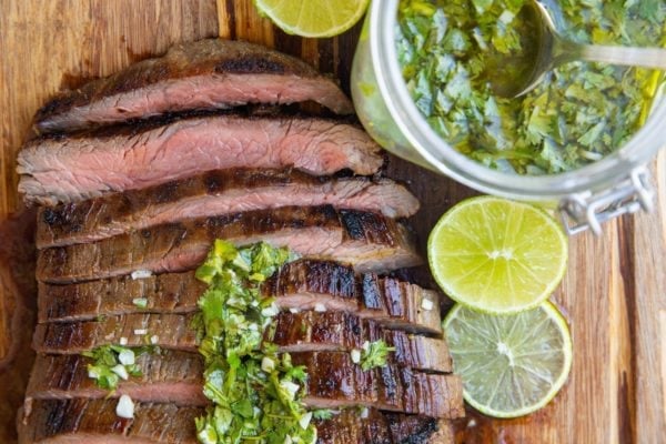 horizontal photo of sliced steak on a cutting board with chimichurri sauce to the side.