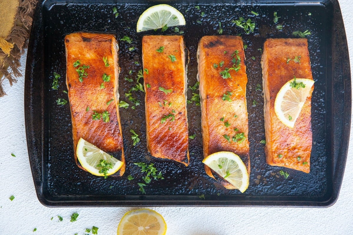 Broiled salmon on a baking sheet with lemon slices and fresh parsley.