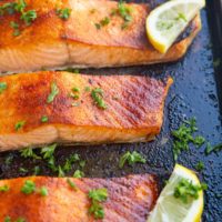 Baking dish with four salmon fillets fresh out of the oven with slices of lemon.