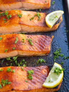 Baking dish with four salmon fillets fresh out of the oven with slices of lemon.
