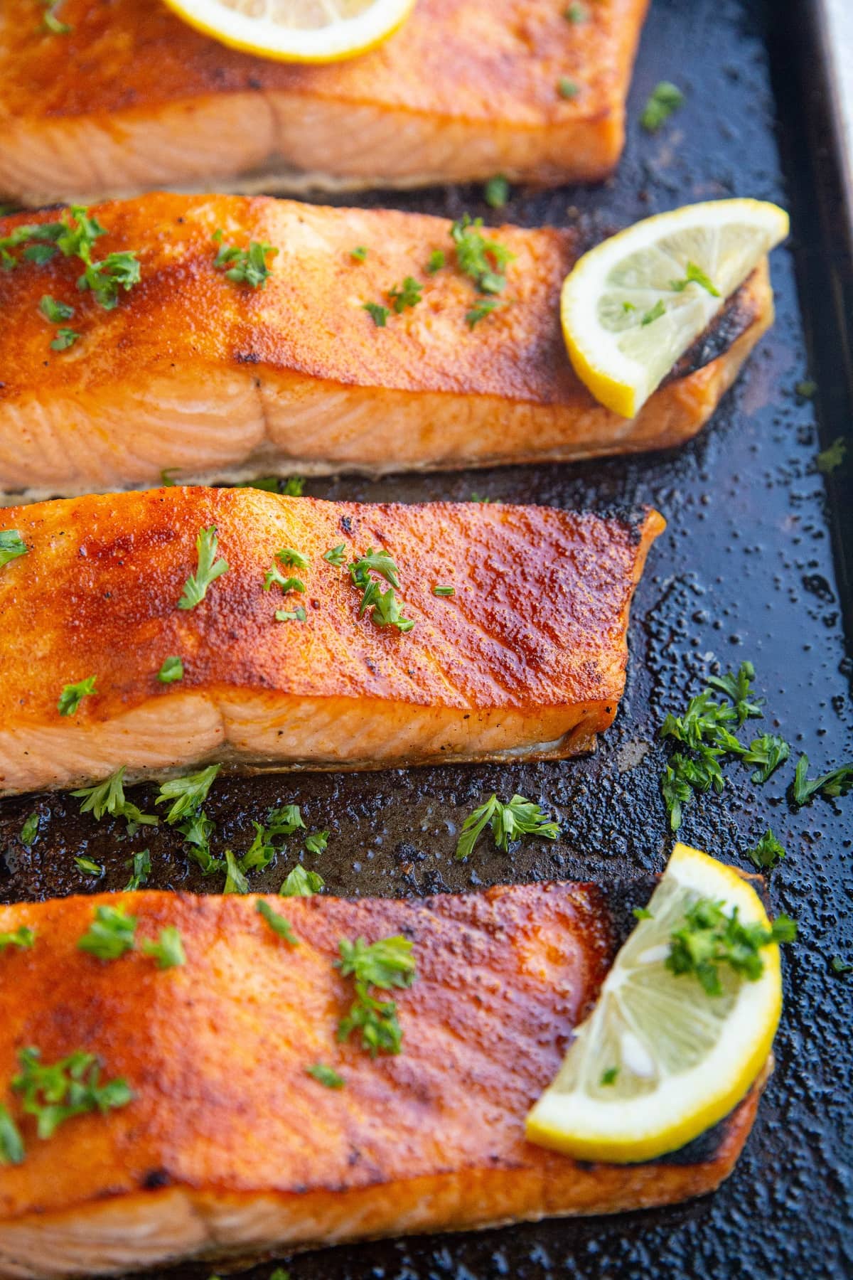 Baking dish with four salmon fillets fresh out of the oven with slices of lemon.