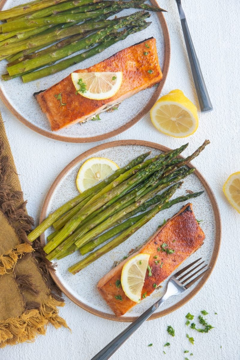 Two plates of baked salmon and asparagus with lemon wedges to the side.