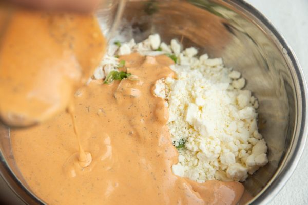 Pouring the sauce into the bowl with the chicken, cheese, and onion