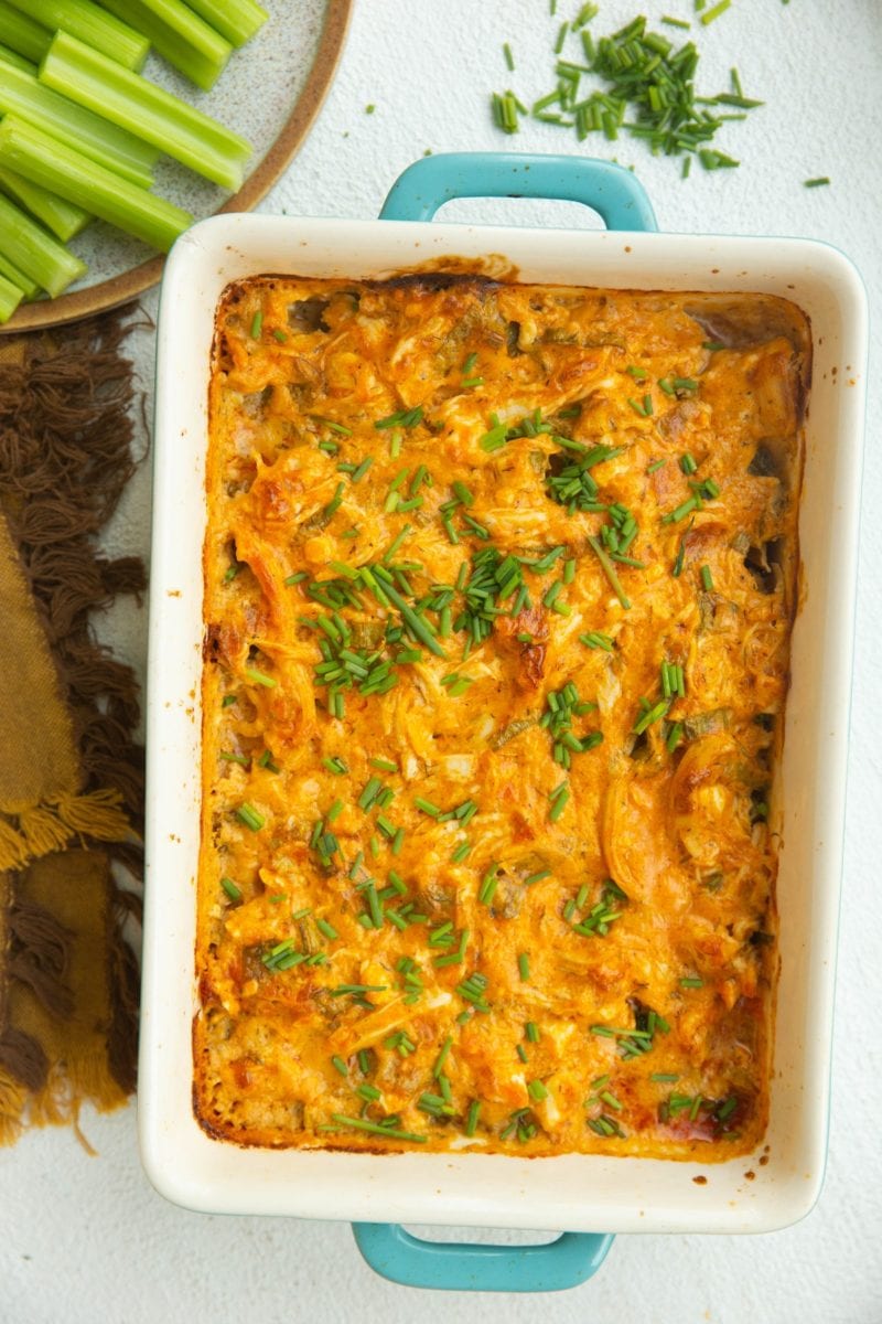 Top down photo of buffalo chicken dip with celery to the side and chives sprinkled on top.