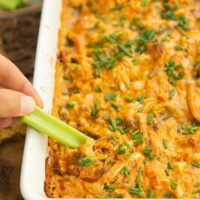 Hand scooping buffalo chicken dip onto a celery stick.