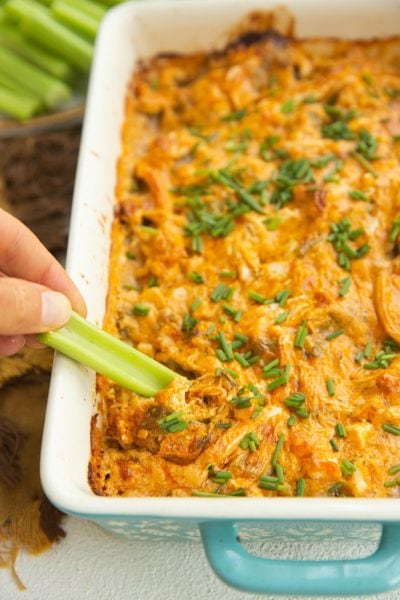 Hand scooping buffalo chicken dip onto a celery stick.