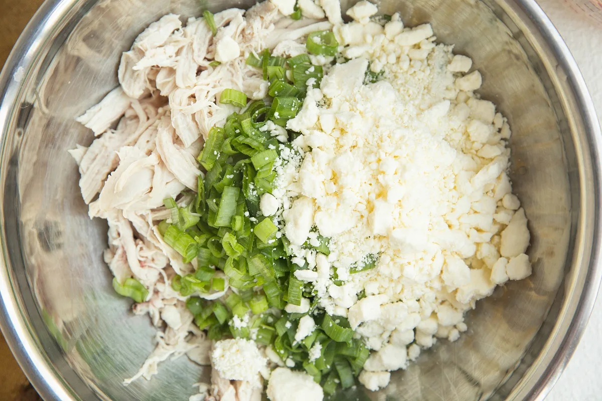Shredded chicken, green onion and feta cheese in a mixing bowl for chicken dip.