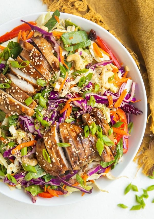 Big bowl of Asian sesame ginger chopped salad with sliced chicken on top and a golden napkin to the side.
