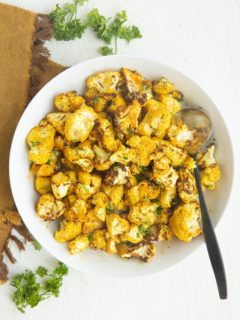 Air fryer cauliflower in a white bowl with a golden napkin to the side, sprinkled with fresh parsley.