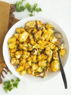 Air fryer cauliflower in a white bowl with a golden napkin to the side, sprinkled with fresh parsley.