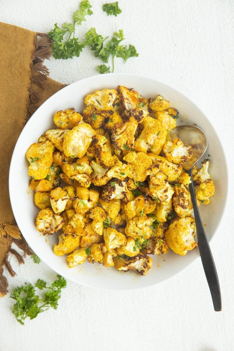 Air fryer cauliflower in a white bowl with a golden napkin to the side, sprinkled with fresh parsley.