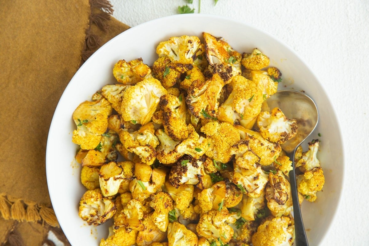 Horizontal photo of curry air fryer cauliflower in a white bowl with a serving spoon.