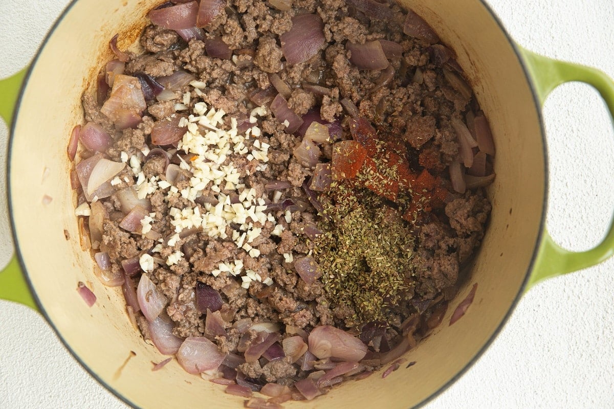 Ground beef and onion cooking in a pot with garlic, oregano and paprika added in.