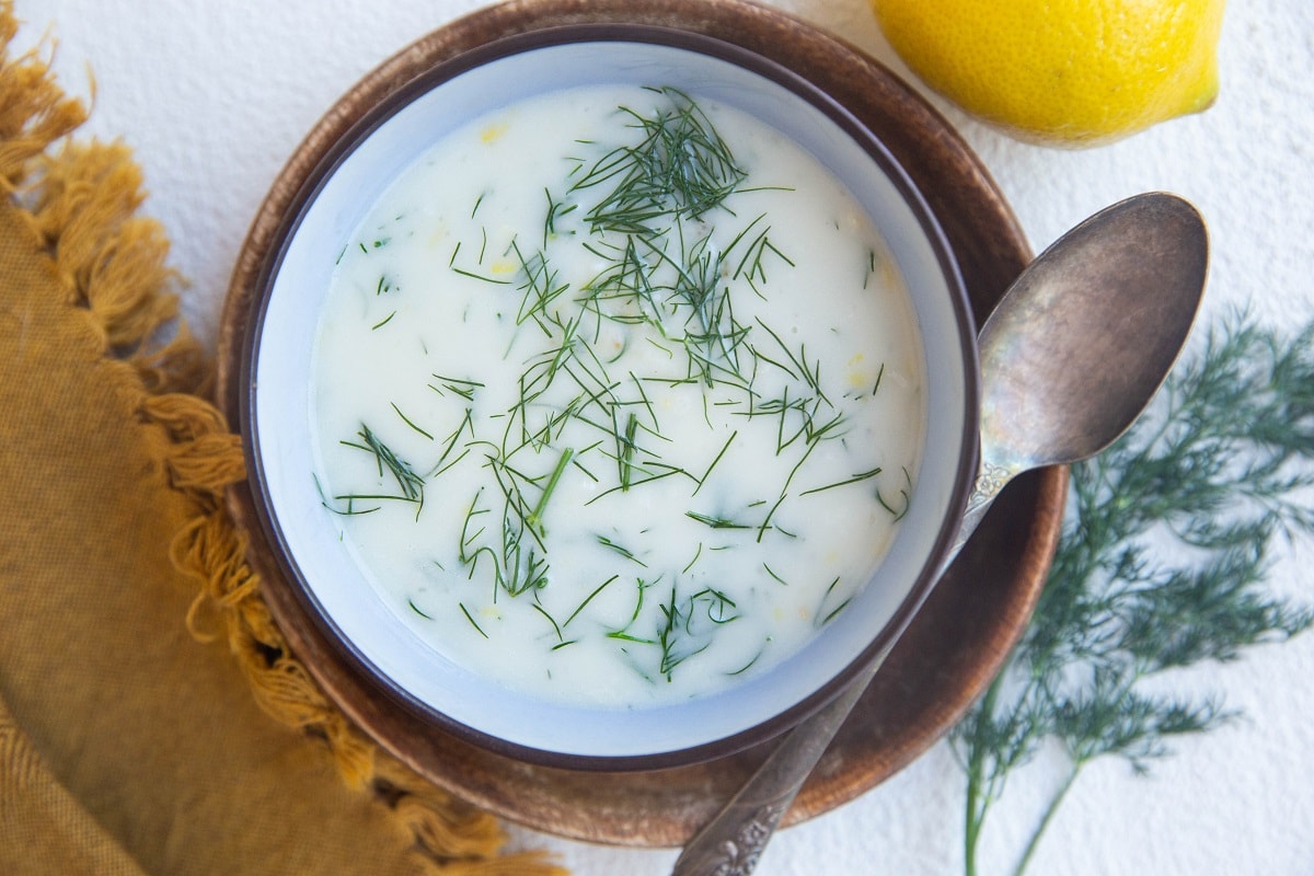 Dairy-Free Dill Sauce For Salmon in a blue bowl on top of a wooden plate with a silver spoon to the side and fresh dill and lemon to the side.