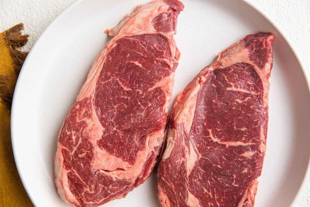 Two New York Strip steaks on a plate, ready to be sliced.