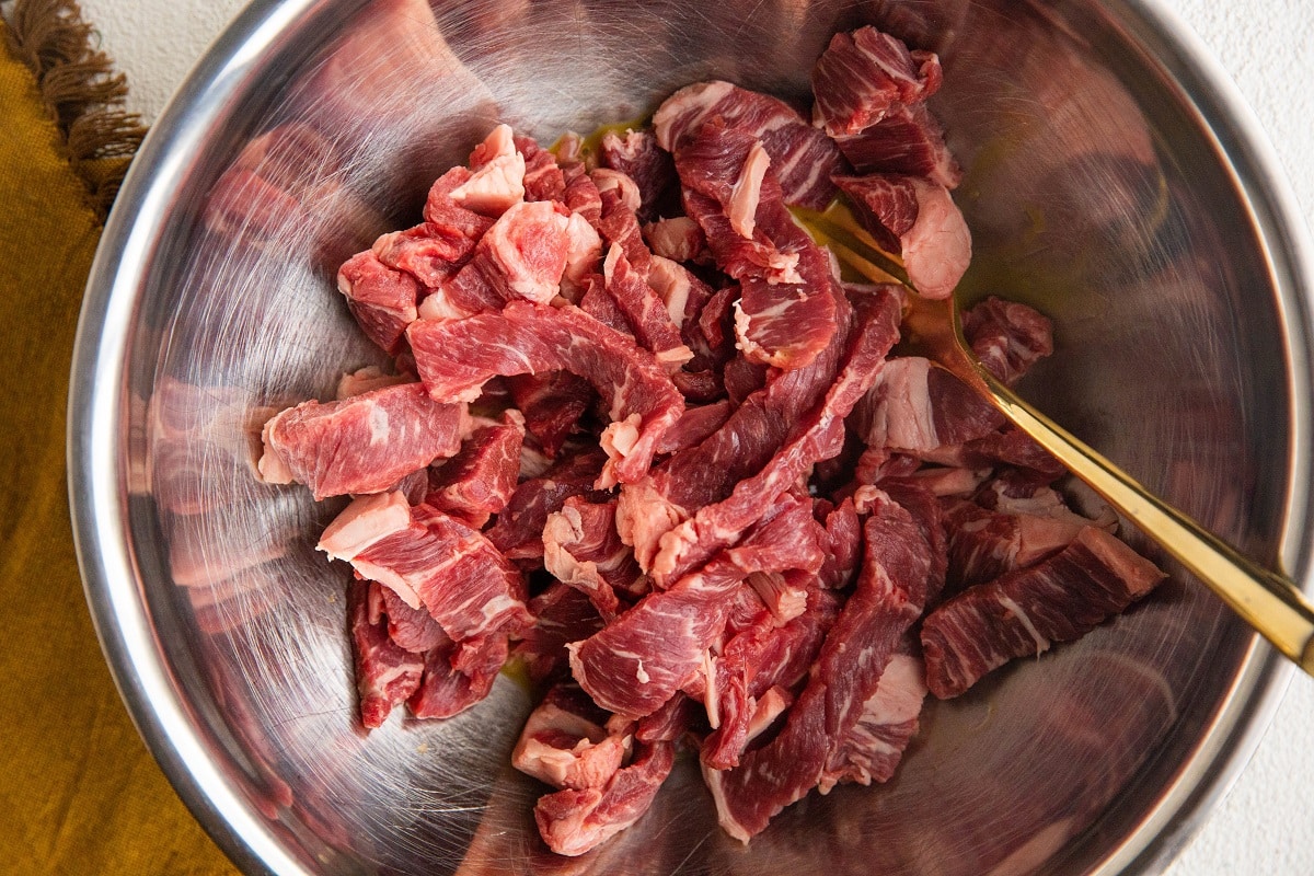 Sliced steak in a mixing bowl with beaten egg