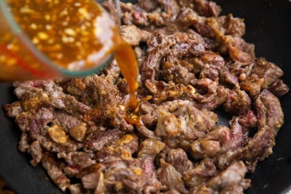 Pouring the orange sauce into the skillet with the beef.