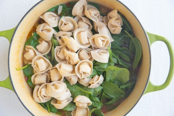 Pot of soup with spinach and tortellini on top