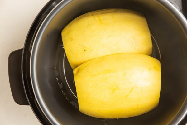 Two halves of a whole spaghetti squash in a pressure cooker, waiting to cook.