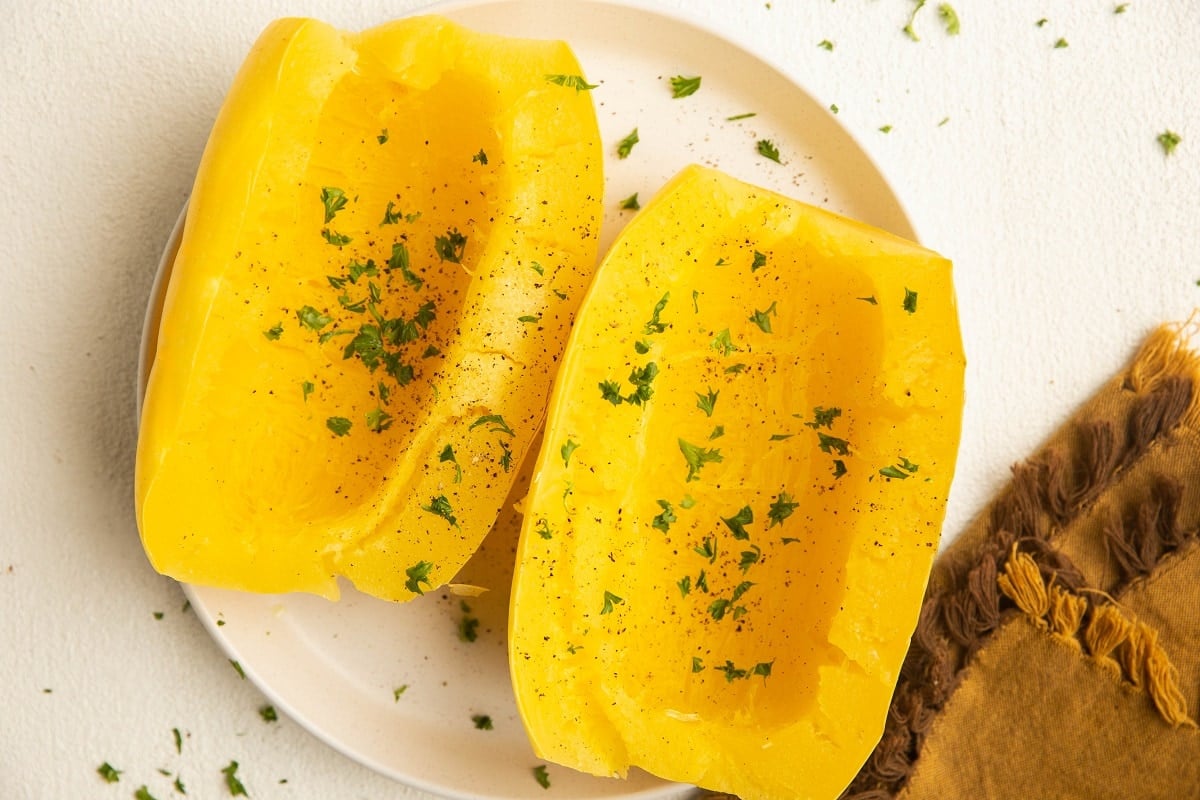 Cooked spaghetti squash on a white plate, sprinkled with pepper and parsley