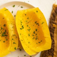 Cooked spaghetti squash on a white plate with a golden napkin to the side.