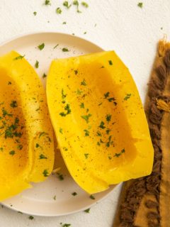 Cooked spaghetti squash on a white plate with a golden napkin to the side.