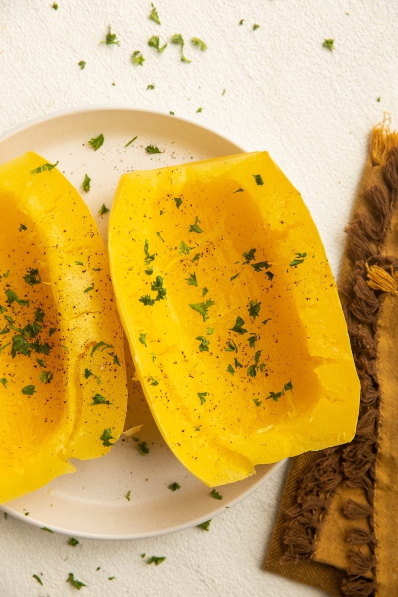 Cooked spaghetti squash on a white plate with a golden napkin to the side.