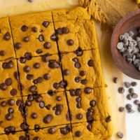 Top down photo of pumpkin baked oats sliced on a sheet of parchment paper with chocolate chips around and a golden frilled napkin.