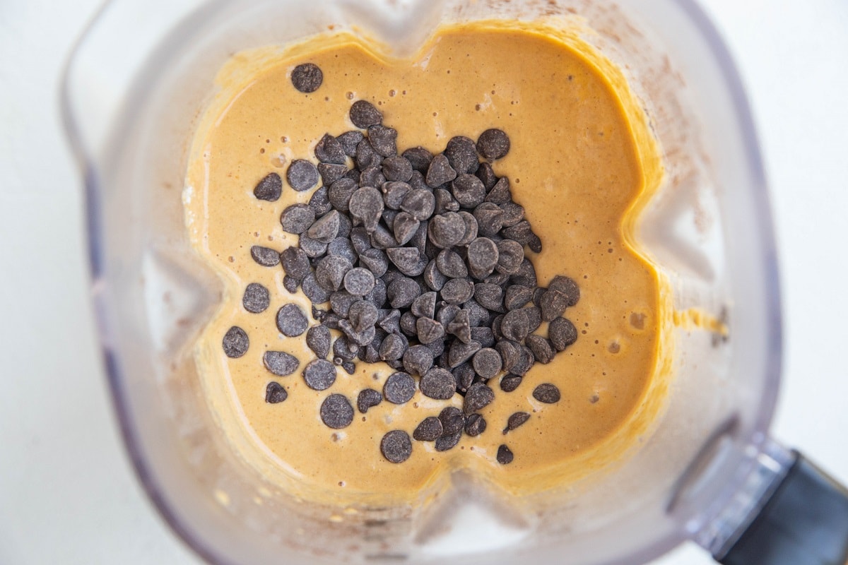 Baked oats batter in a blender with chocolate chips on top to be stirred in.