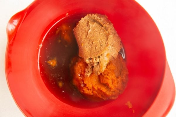 Red mixing bowl with pumpkin puree, almond butter and pure maple syrup inside.