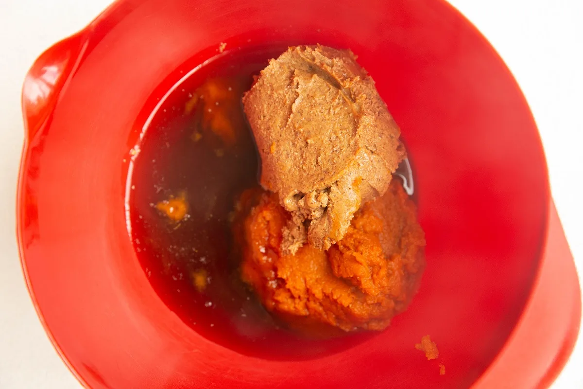Red mixing bowl with pumpkin puree, almond butter and pure maple syrup inside.