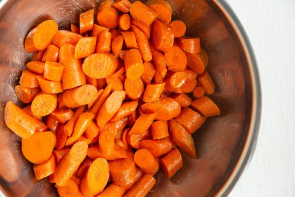 Carrots in a mixing bowl coated with oil and seasoning.